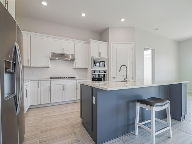 kitchen featuring white cabinetry, stainless steel appliances, under cabinet range hood, a kitchen bar, and tasteful backsplash