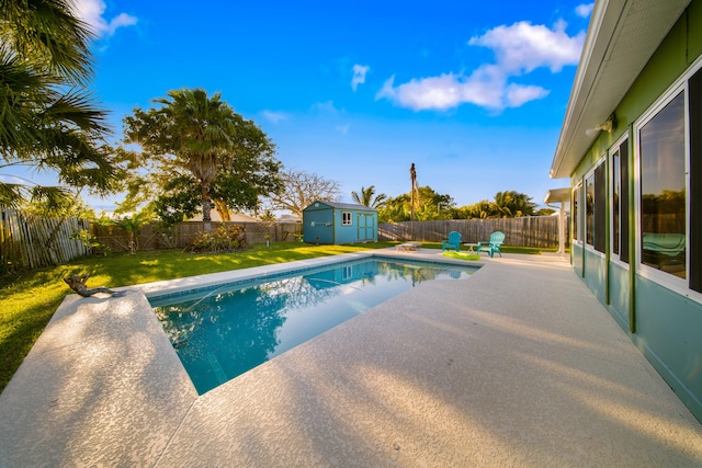 view of swimming pool featuring a storage unit, a fenced backyard, and a yard