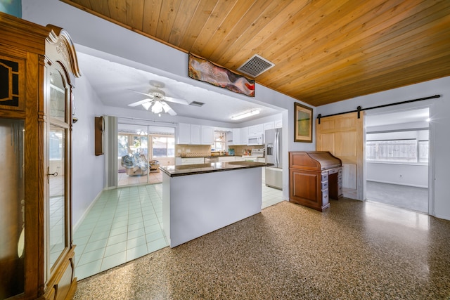 kitchen with wooden ceiling, a barn door, stainless steel fridge, dark countertops, and visible vents