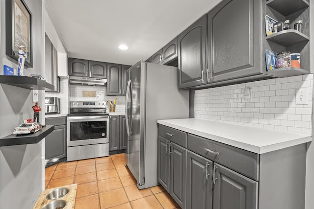 kitchen featuring under cabinet range hood, light tile patterned floors, decorative backsplash, gray cabinets, and appliances with stainless steel finishes