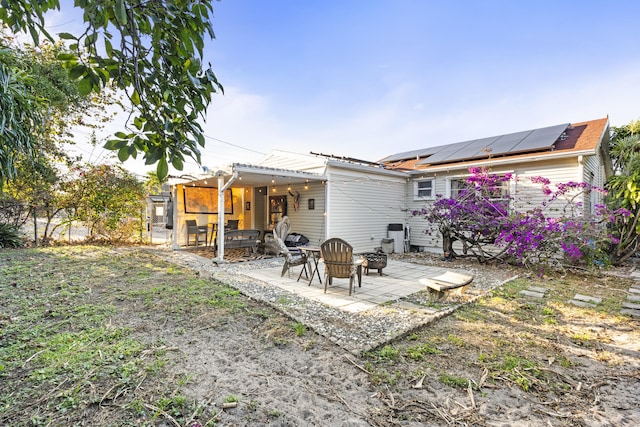 rear view of house featuring roof mounted solar panels, an outdoor fire pit, and a patio