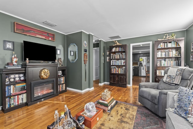 living area with visible vents, baseboards, ornamental molding, wood finished floors, and a glass covered fireplace