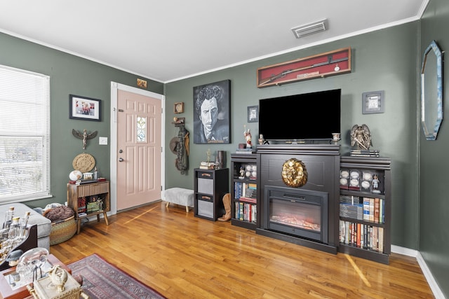 living room with visible vents, ornamental molding, a glass covered fireplace, wood finished floors, and plenty of natural light