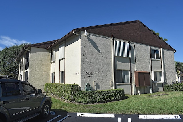 view of property exterior with stucco siding, a yard, and uncovered parking