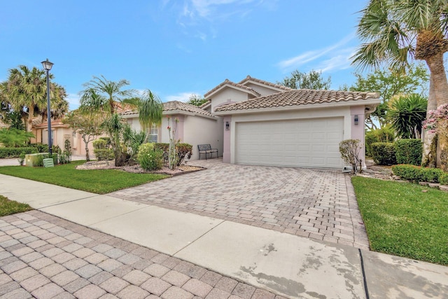 mediterranean / spanish-style home featuring stucco siding, a tiled roof, decorative driveway, and a garage