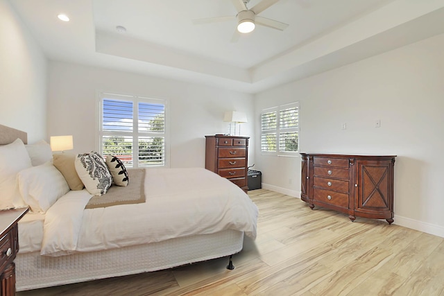 bedroom featuring a tray ceiling, multiple windows, light wood-style floors, and baseboards