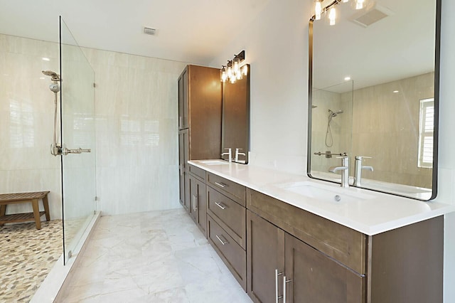 full bathroom with double vanity, marble finish floor, a tile shower, and a sink