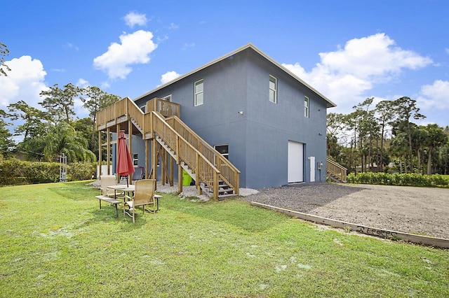 rear view of property featuring gravel driveway, stairway, a wooden deck, a garage, and a yard