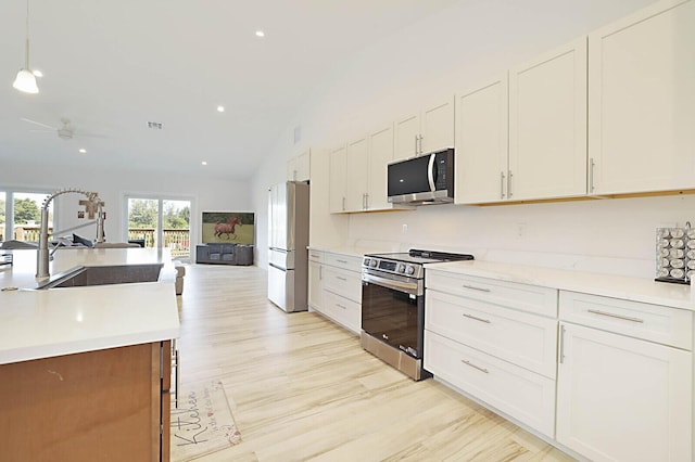 kitchen featuring light wood-style flooring, a sink, appliances with stainless steel finishes, white cabinetry, and open floor plan