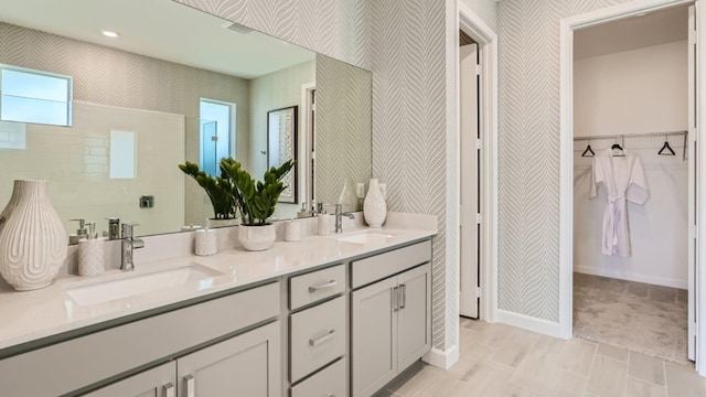 bathroom featuring double vanity, a sink, a walk in closet, and wallpapered walls