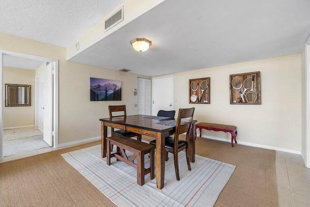 dining space with light tile patterned floors, visible vents, baseboards, and a textured ceiling