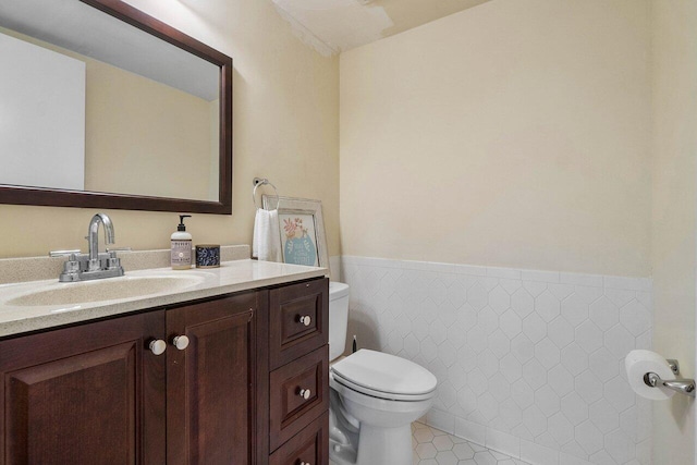 half bath with tile patterned flooring, tile walls, toilet, wainscoting, and vanity