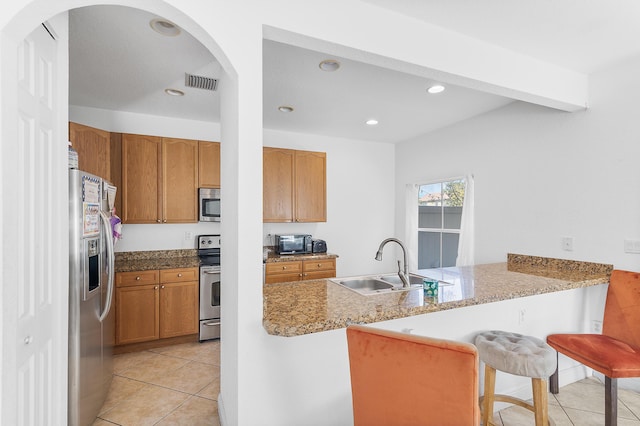 kitchen with a peninsula, recessed lighting, a sink, stainless steel appliances, and a kitchen bar