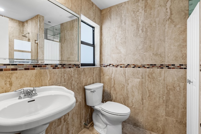 full bathroom featuring tile walls, toilet, tiled shower, and a sink