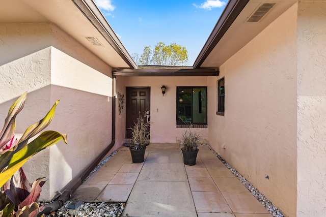 view of exterior entry with a patio area, visible vents, and stucco siding