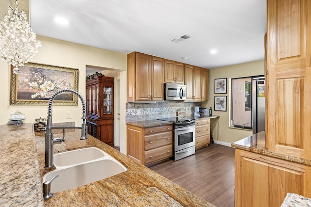 kitchen with light stone countertops, dark wood-style flooring, a sink, stainless steel appliances, and tasteful backsplash