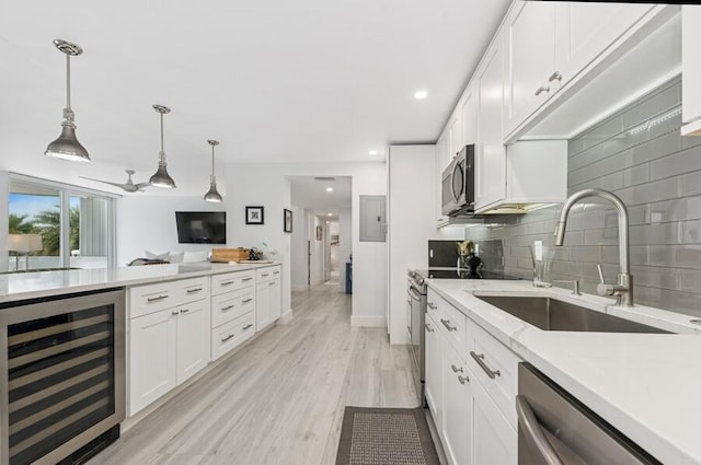 kitchen featuring wine cooler, decorative backsplash, white cabinets, stainless steel appliances, and a sink