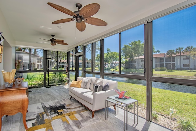 sunroom with plenty of natural light, a ceiling fan, and a water view