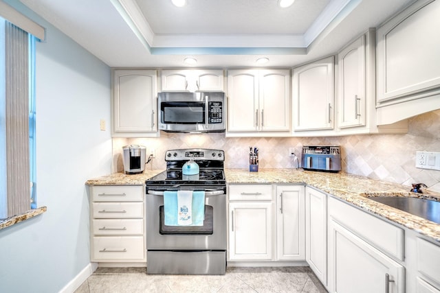 kitchen featuring ornamental molding, light stone counters, a tray ceiling, backsplash, and appliances with stainless steel finishes