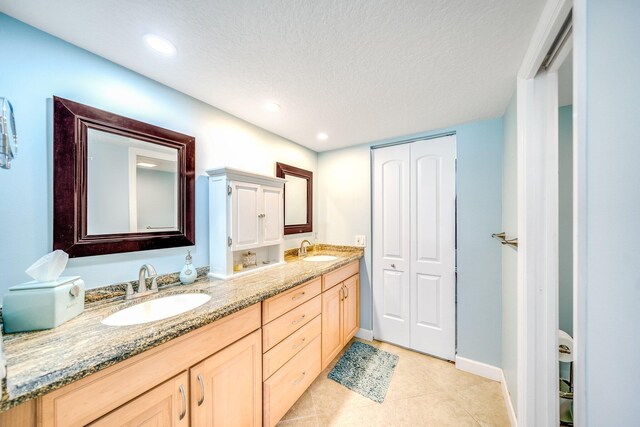 bathroom with a textured ceiling, double vanity, tile patterned flooring, and a sink