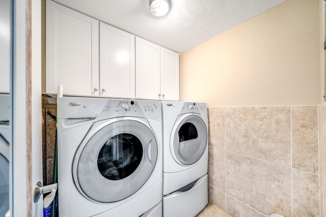 laundry room featuring tile walls, washing machine and dryer, wainscoting, cabinet space, and a textured ceiling