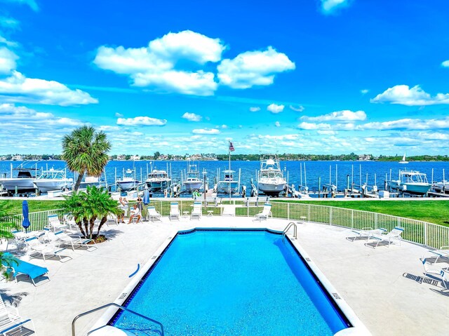 pool with a patio area, a water view, and fence