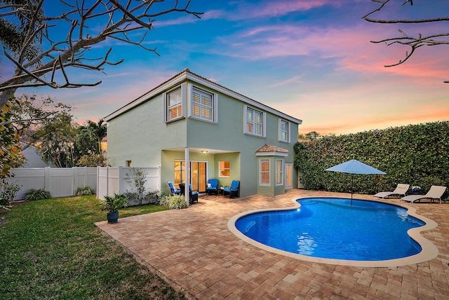 pool at dusk featuring a fenced in pool, a lawn, a fenced backyard, and a patio area