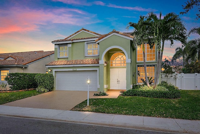 mediterranean / spanish-style house with stucco siding, a lawn, decorative driveway, fence, and a garage