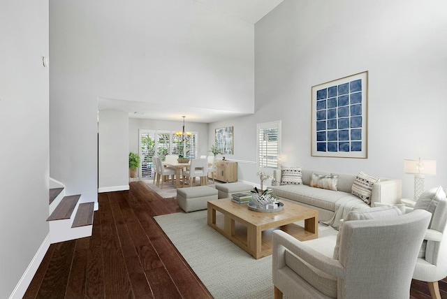 living area with a high ceiling, wood finished floors, baseboards, and a chandelier