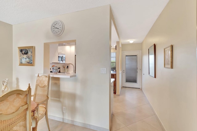 hall featuring light tile patterned flooring, baseboards, and a sink