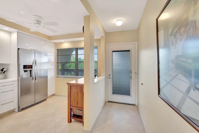 doorway to outside with light tile patterned floors, a textured ceiling, baseboards, and a ceiling fan