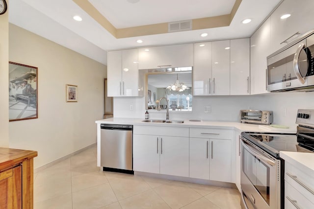 kitchen with visible vents, light countertops, a tray ceiling, stainless steel appliances, and a sink