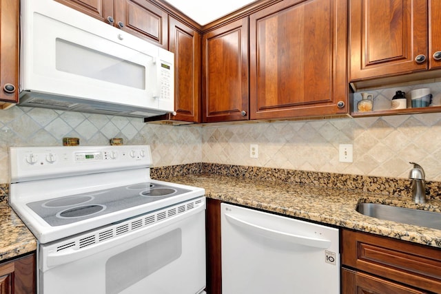 kitchen with a sink, white appliances, tasteful backsplash, and light stone counters