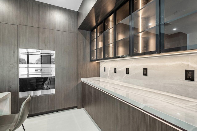 kitchen with decorative backsplash, double oven, modern cabinets, and glass insert cabinets