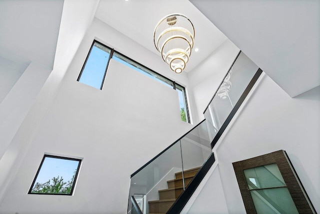 stairway with a notable chandelier, plenty of natural light, and a towering ceiling