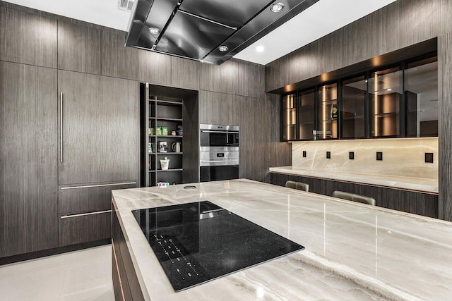 8387 Sawpine Rd, Delray Beach, FL 33446 - kitchen with light stone counters, black electric cooktop, glass insert cabinets, double oven, and dark brown cabinets