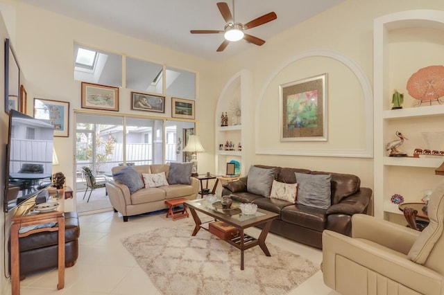 living area featuring built in shelves, a ceiling fan, a high ceiling, a skylight, and light tile patterned flooring