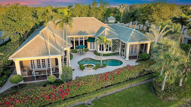 back of property at dusk with an outdoor pool, french doors, a patio, and a sunroom