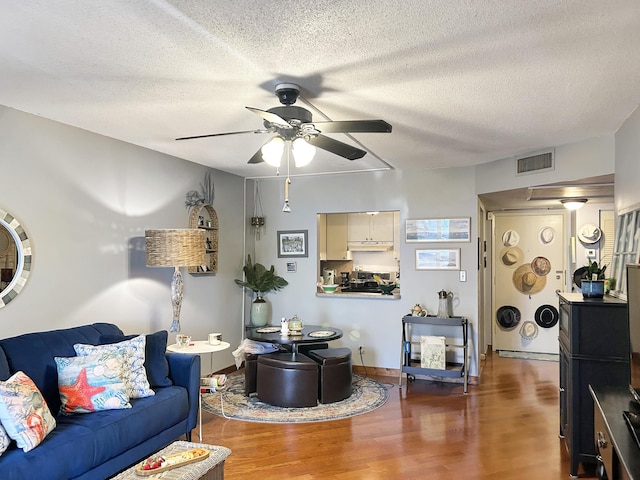 living area with visible vents, a textured ceiling, a ceiling fan, and wood finished floors