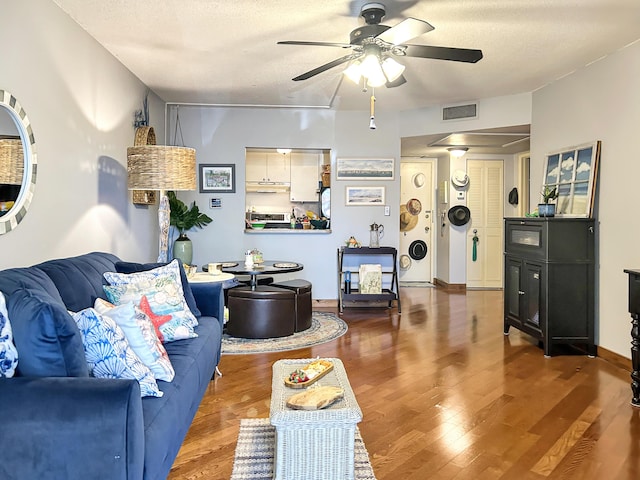 living area featuring visible vents, a textured ceiling, a ceiling fan, and wood finished floors