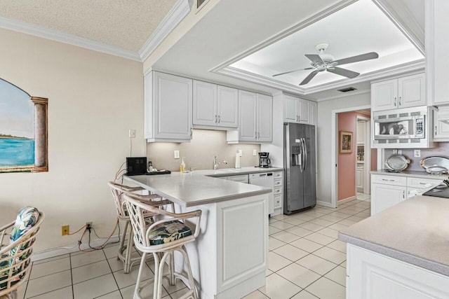 kitchen with ornamental molding, a tray ceiling, stainless steel appliances, a peninsula, and white cabinets