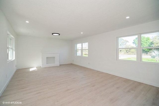 empty room featuring recessed lighting, a fireplace, baseboards, and light wood finished floors