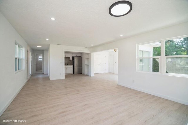 unfurnished living room with recessed lighting, baseboards, and light wood finished floors