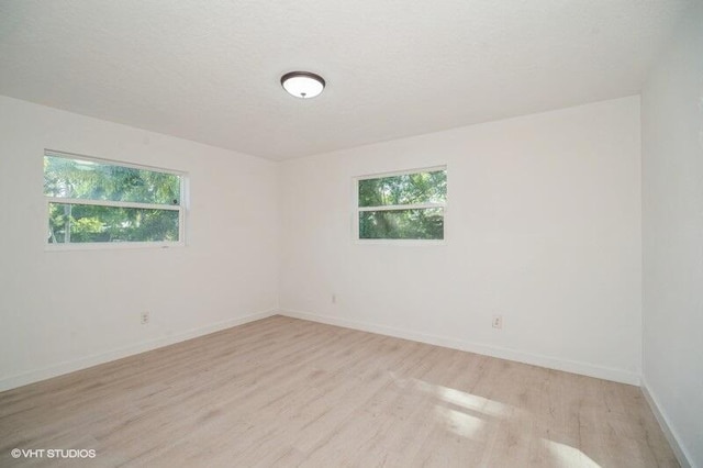 unfurnished room with plenty of natural light, a textured ceiling, baseboards, and light wood-style floors