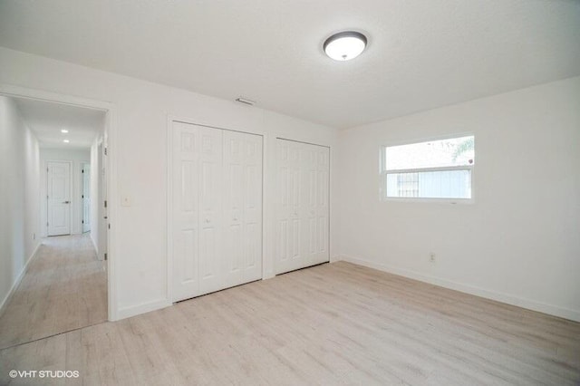 unfurnished bedroom featuring wood finished floors, baseboards, and two closets