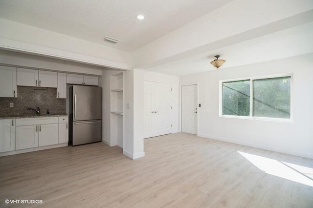 kitchen with backsplash, visible vents, light wood-style flooring, and freestanding refrigerator