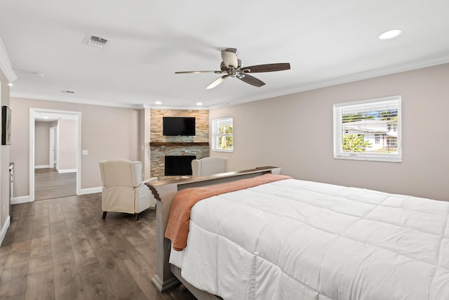 bedroom with visible vents, dark wood-type flooring, a stone fireplace, and crown molding