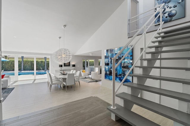 dining room featuring stairway, high vaulted ceiling, an inviting chandelier, and wood finished floors