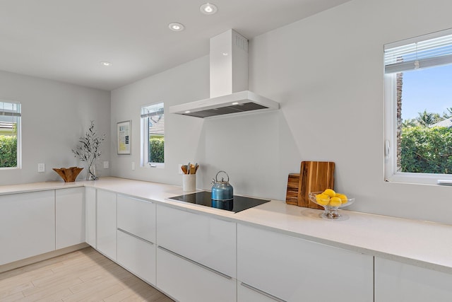 kitchen featuring modern cabinets, wall chimney range hood, white cabinets, light countertops, and black electric stovetop