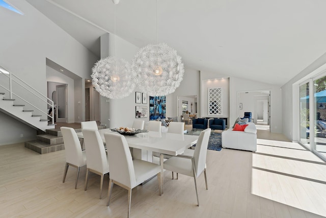 dining area with high vaulted ceiling, a notable chandelier, stairs, and light wood finished floors